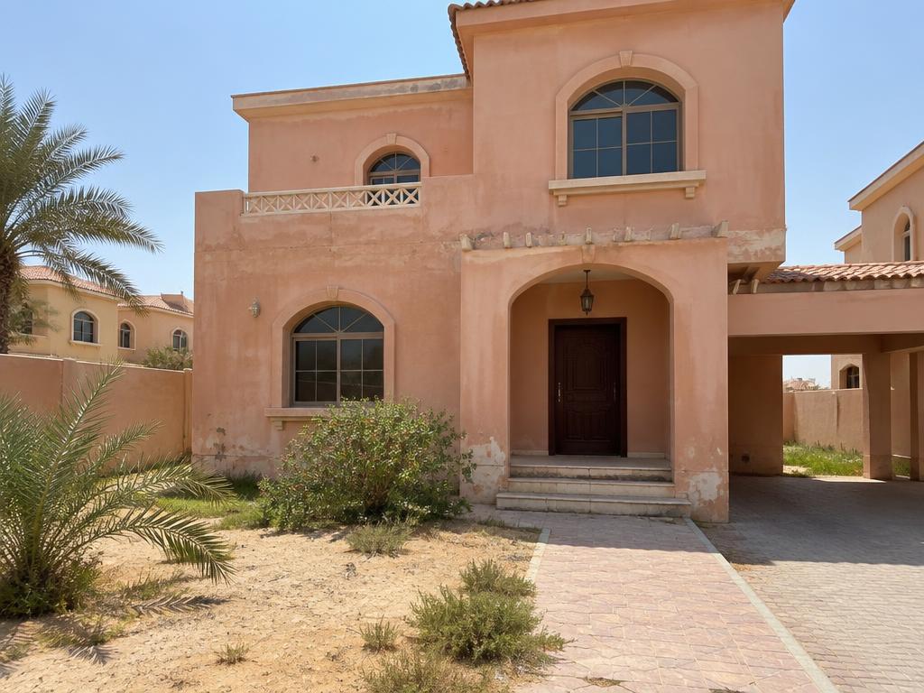 Faded peach villa exterior and sparse front garden before renovation in Al Hamra Village